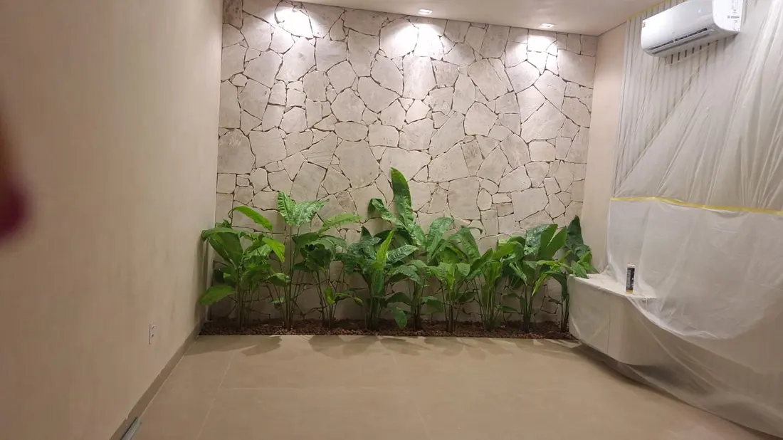 Jardim interno coberto com parede de pedra e iluminação embutida