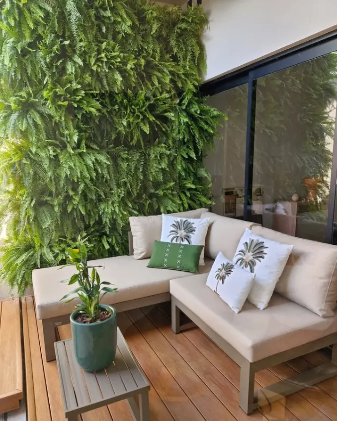 Muro verde com samambaias, sofá e deck de madeira em área externa